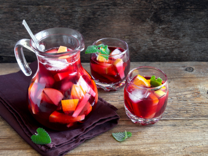 A pitcher and two glasses of red wine sangria with sliced fruits and mint