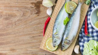 Fresh sardines with halved lemons and coriander leaf surrounded with ginger, red chilies, and garlic on a wooden table