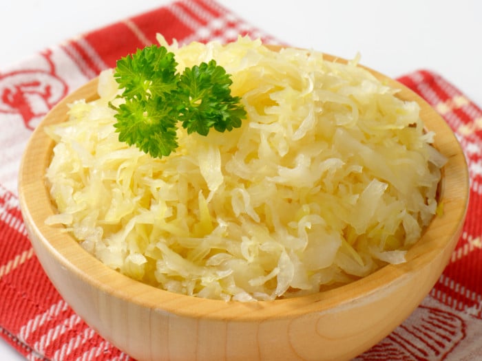 A wooden bowl of sauerkraut on a red kitchen napkin