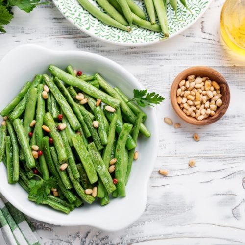 A flat lay picture of sauteed green beans in a white bowl kept atop a white platform