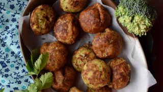 Flatline view of a tray of muffins with a broccoli head and coriander leaves kept on either side