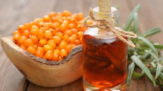 A close-up shot of a bottle containing seabuckthorn oil kept in front of a basket of seabuckthorn