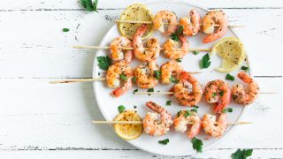 Grilled shrimp on skewers on lemon slices on a white plate