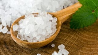 A wooden spoon filled with sea salt - crystalline pebbles and leaves on a wooden table