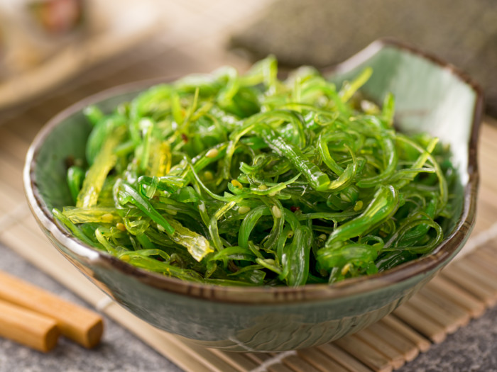 A bowl of stir-fried wakame seaweed on a wooden mat