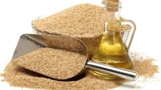 A bowl and scoop of sesame seeds with a jar of sesame oil on a white background