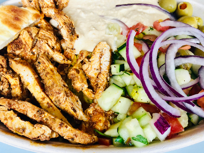 Mediterranean Chicken Shawarma Rice Bowl with Hummus Greek Salad Olives and Pita Bread Top View on Table
