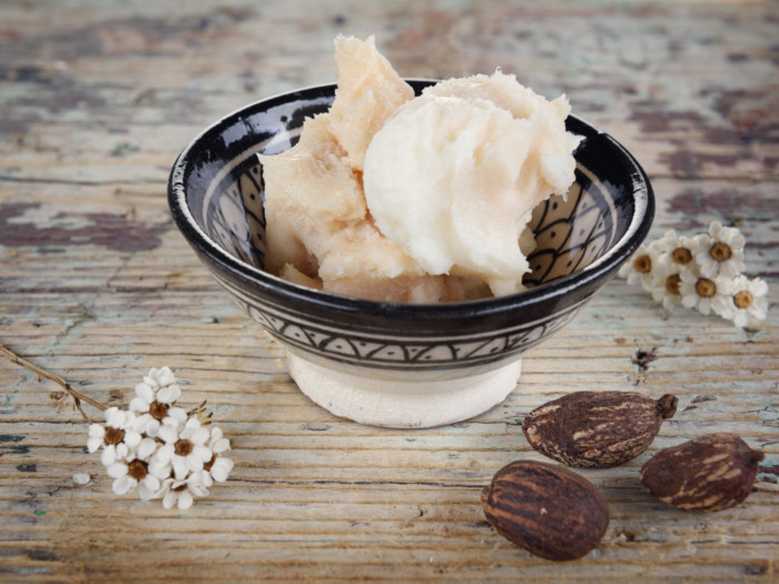 A bowl containing shea butter kept on a wooden platform next to flowers and shea nuts