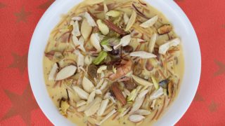 Sheer khurma with nuts in a white bowl against red background