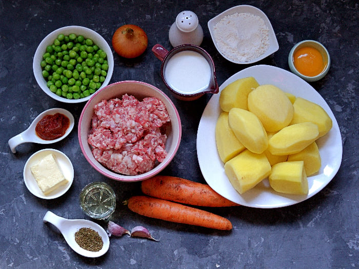 Ingredients for a "shepherd's pie", the British potato casserole with minced meat and vegetables. Peeled potatoes, minced meat, butter, milk, flour, egg yolk, carrots, green peas, onion, garlic, salt