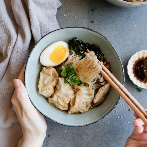 A person using chopsticks to have shirataki soup noodles with gyoza