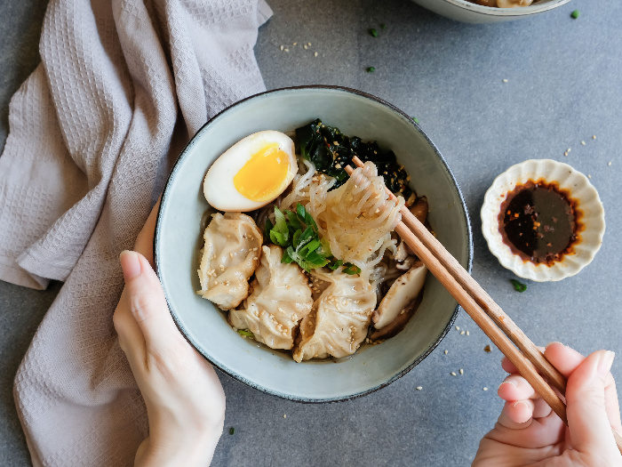 A person using chopsticks to have shirataki soup noodles with gyoza