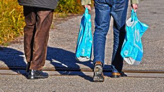 Two people walking on the street carrying plastic shopping bags