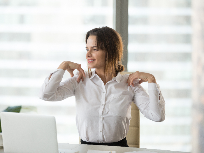 Smiling woman sitting at a desk with her fingers touching her shoulders
