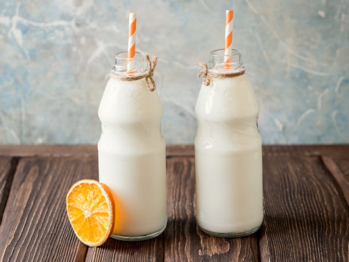 2 bottles fresh skimmed milk with orange striped straws and a slice of lime kept on a wooden table