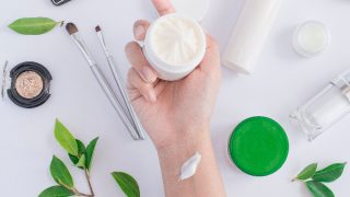 A hand holding a small container of cream against a white background