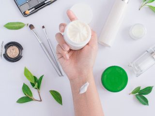 A hand holding a small container of cream against a white background