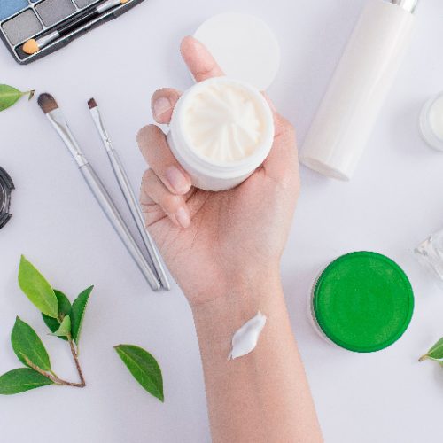 A hand holding a small container of cream against a white background