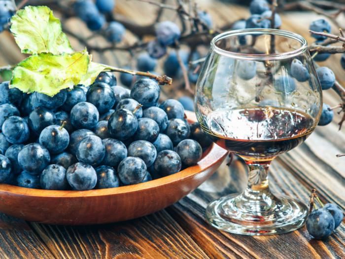 A glass of sloe gin kept next to a bowl of sloe berries kept atop a wooden table