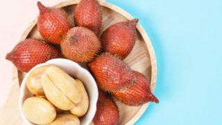 Peeled salak in a white bowl on top of unpeeled salak fruits