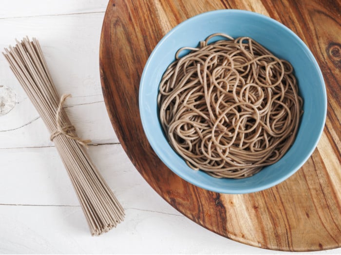 Cooked soba noodles in a bowl and dried soba noodles tied in twine