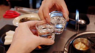 Two shots of soju in glasses being held