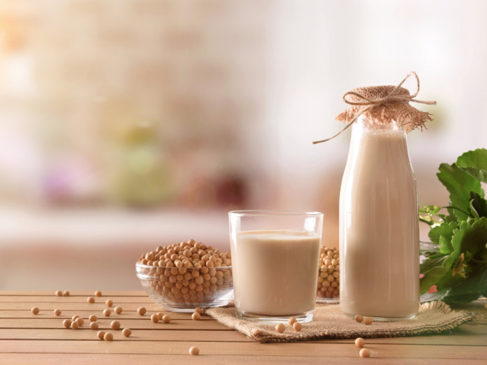 A bowl of soy seeds with a glass and jar of soymilk on a wooden table