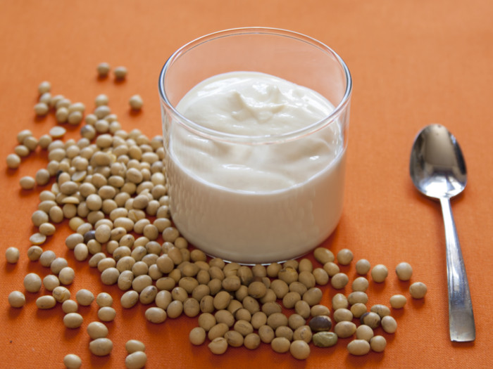 Soy yogurt in a glass bowl with a spoon and soybeans next to it
