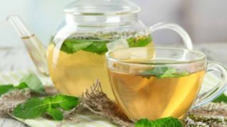 A kettle and cup of spearmint tea surrounded with fresh spearmint leaves on a cloth