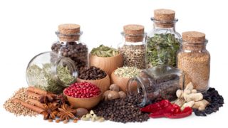 Bottles of dried, whole spices stacked next to each other, against a white background
