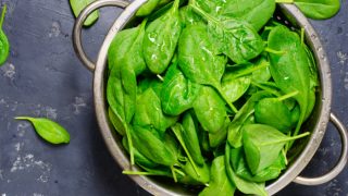 A bowl of spinach leaves on a gray background