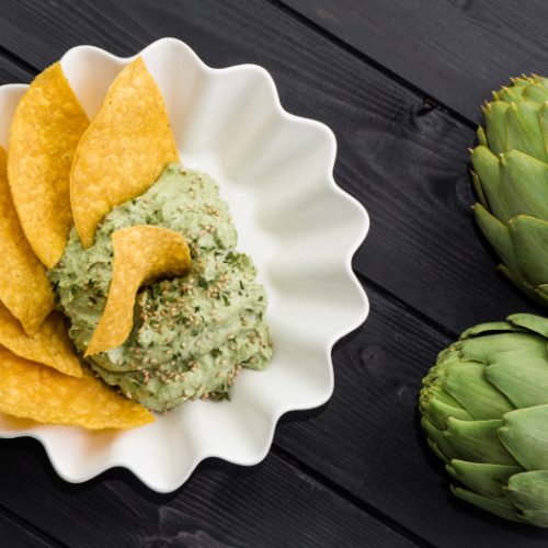 Homemade dip with corn nachos and artichokes on the black wooden background