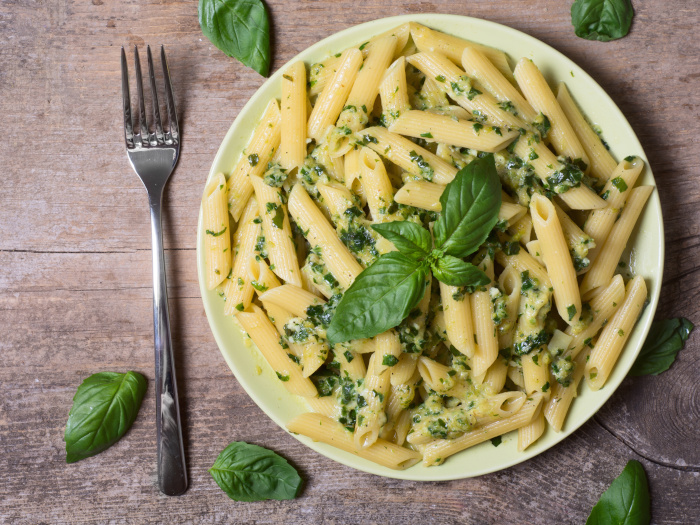 Penne pasta with spinach pesto sauce and green basil on a plate