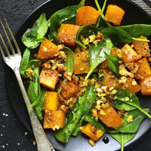 Roasted pumpkin salad with spinach and walnut on a black plate