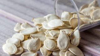 A close-up shot of squash seeds falling out of a glass container onto a wooden platform