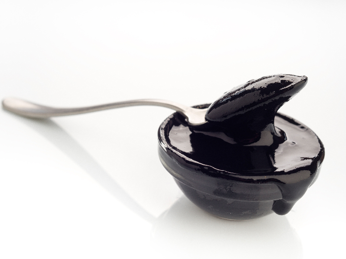 Spoon with concentrated paste squid ink on white background