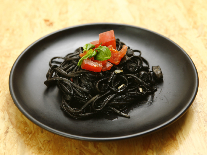 A close up shot of a plate of squid ink pasta kept atop a wooden platform