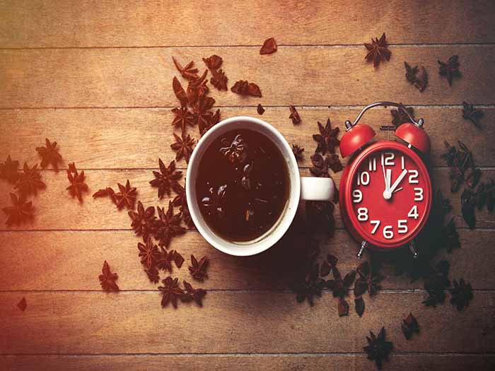 A flat-lay picture of star anise tea surrounded by star anise spices and a red table clock