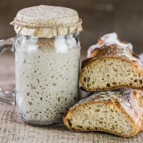 Two loaves of sourdough breads with a bottle of starter