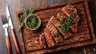 Steak, sauce, and some twigs of an herb with knife and fork on a table