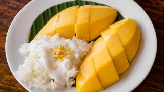 Mango, coconut meat, and sticky rice on a banana leaf on a white dish