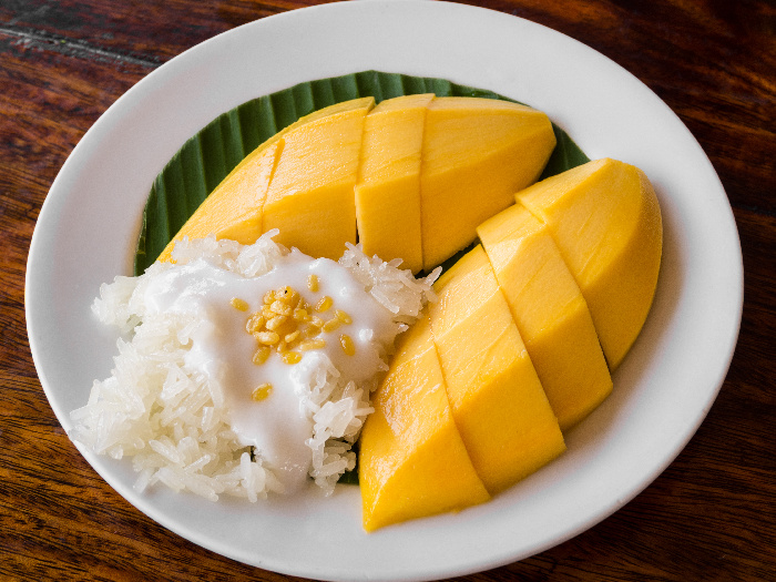 Mango, coconut meat, and sticky rice on a banana leaf on a white dish