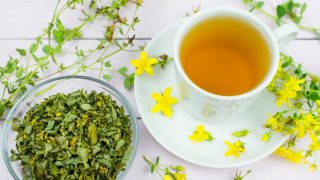 A cup of St John's wort tea kept next to a bowl of St. John's wort herb