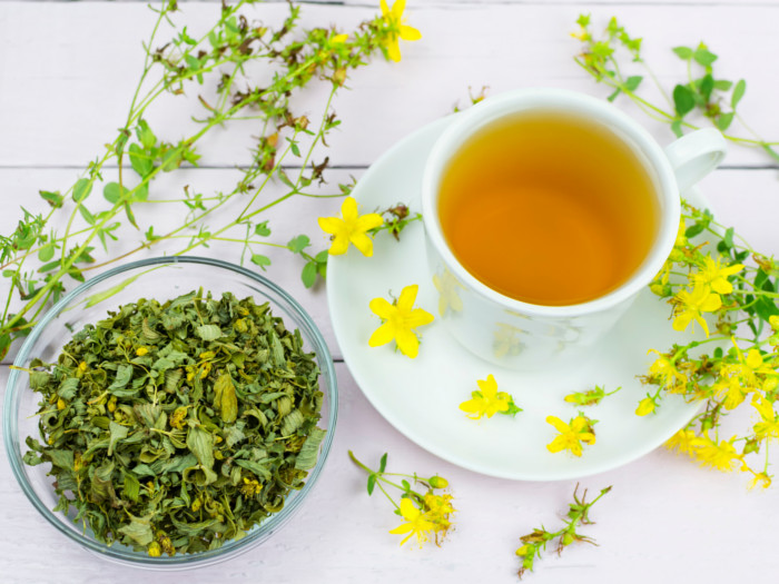 A cup of St John's wort tea kept next to a bowl of St. John's wort herb