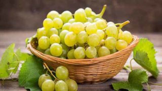 A basket of green grapes on a wooden table