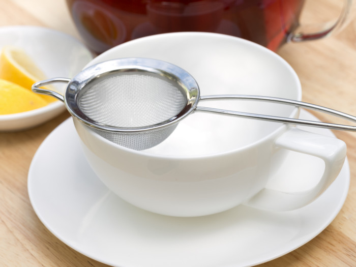 A teacup with a tea strainer and lemon slices in the background