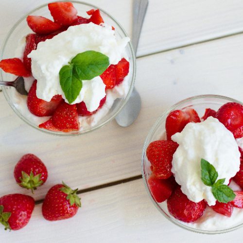Strawberries and cream in a bowl kept atop a table, next to three red strawberries