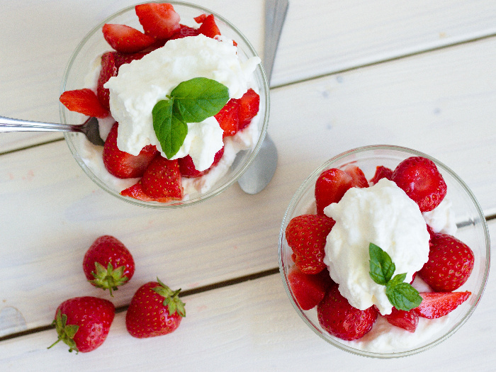 Strawberries and cream in a bowl kept atop a table, next to three red strawberries