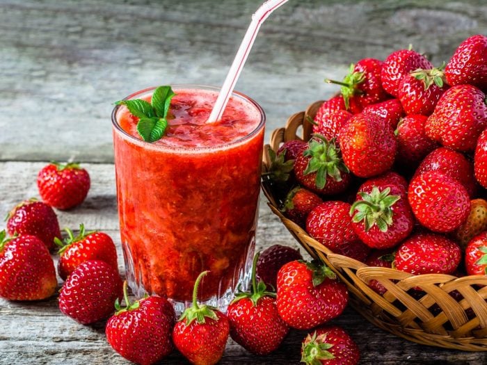 A glass of fresh strawberry juice kept beside a basket of juicy strawberries