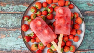 2 strawberry popsicles along with fresh strawberries on a plate